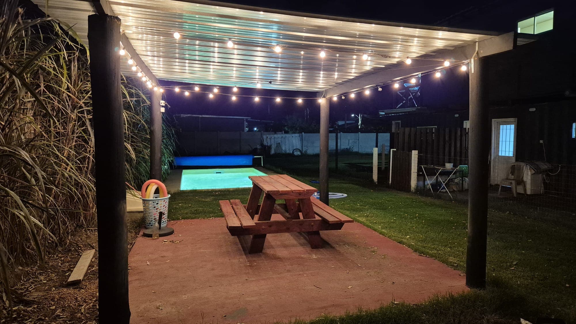 Pérgola con luces colgantes y pileta iluminada en el complejo Marinas Playa Grande
